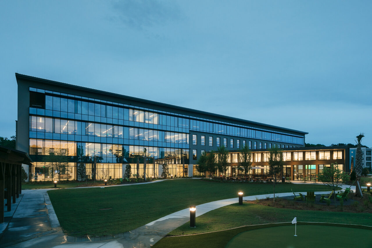 Modern glass office building lit up at dusk with a landscaped lawn.