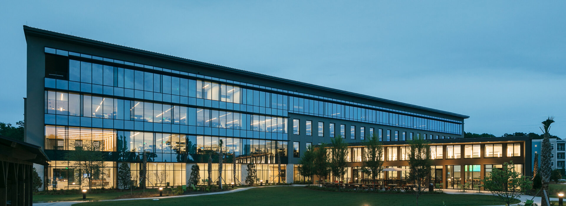 Modern glass office building lit up at dusk with a landscaped lawn.