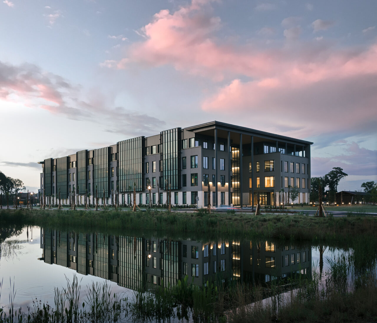 Modern office building reflected in a pond at sunset with pink clouds in the sky.