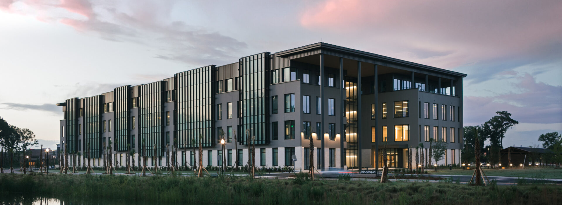 Modern office building reflected in a pond at sunset with pink clouds in the sky.