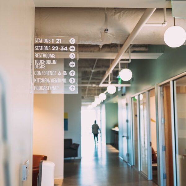 Modern coworking space hallway with directional signage and pendant lights.