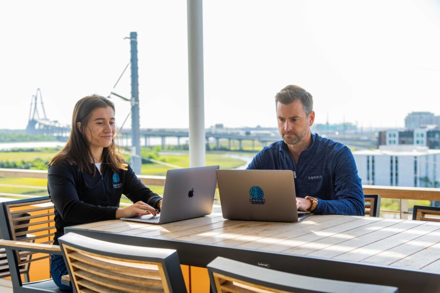 Man and woman from Gnosis working on laptops on a terrace overlooking Charleston.