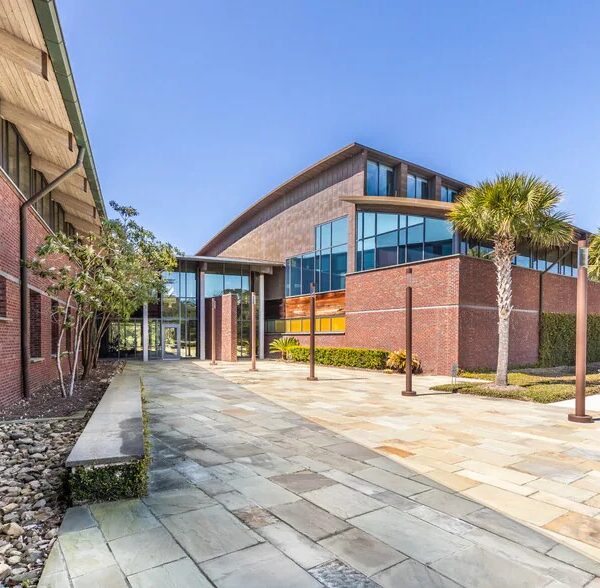 Modern brick building with a curved roof, courtyard, and palm trees.