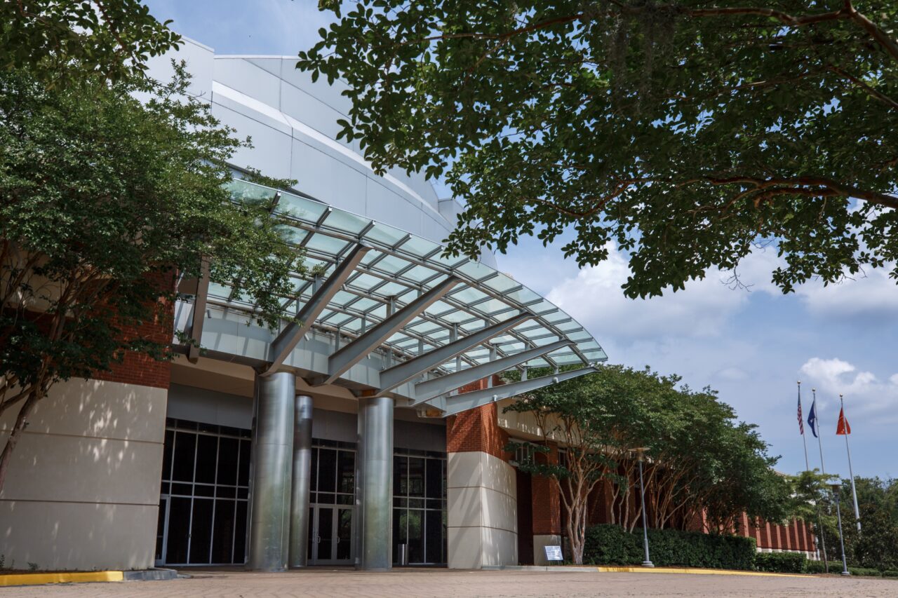 Modern building entrance with a curved glass canopy and steel columns.