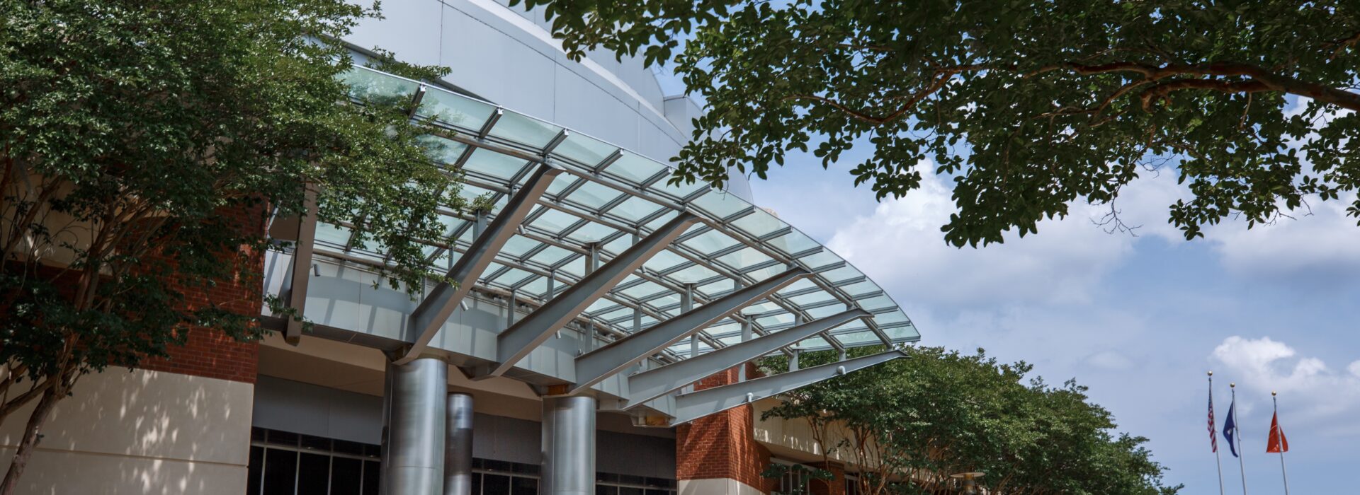 Modern building entrance with a curved glass canopy and steel columns.