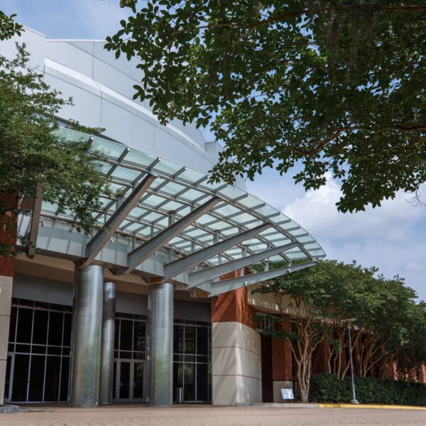 Modern building entrance with a curved glass canopy and steel columns.
