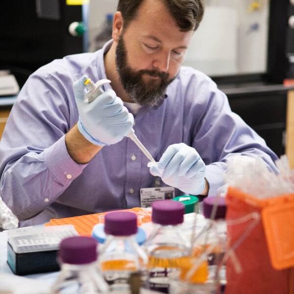 Scientist using a pipette to transfer liquid samples in a laboratory.