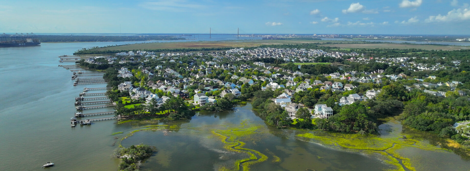 Aerial view of a waterfront residential neighborhood with marsh, private docks, and a bridge in the distance.