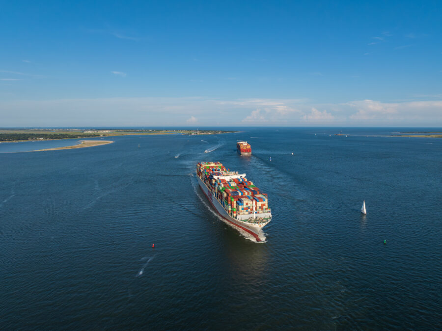 Cargo ship loaded with containers heading out to sea past a coastline.