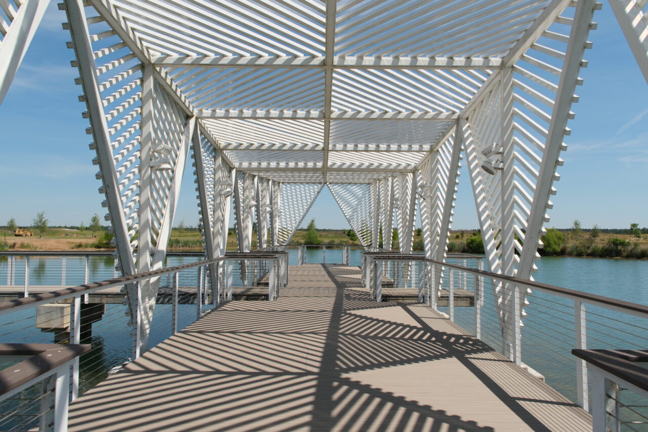 Modern white pedestrian bridge with geometric slatted structure crossing a lake.