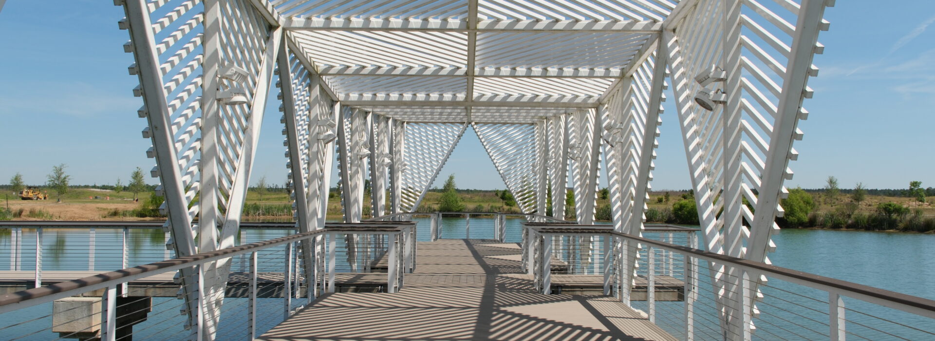 Modern white pedestrian bridge with geometric slatted structure crossing a lake.