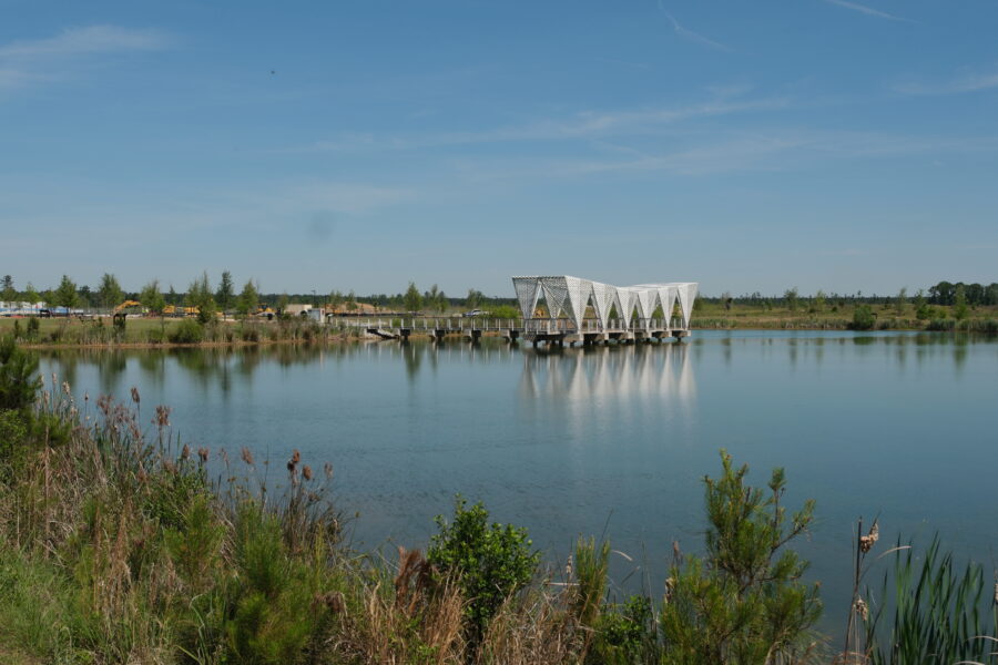 White architectural pavilion and pier on a calm lake under a blue sky.