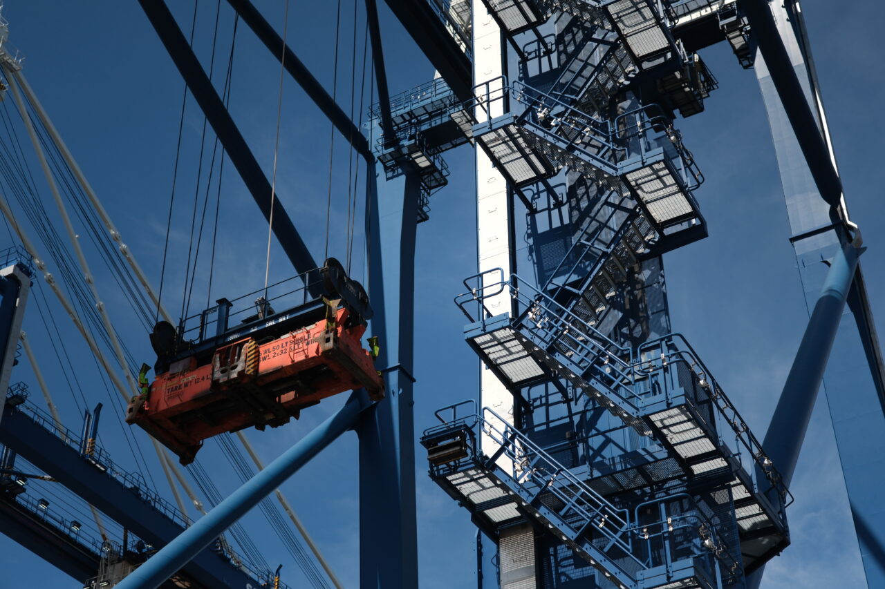 Detail of a port crane's lifting mechanism and steel structure against a blue sky.