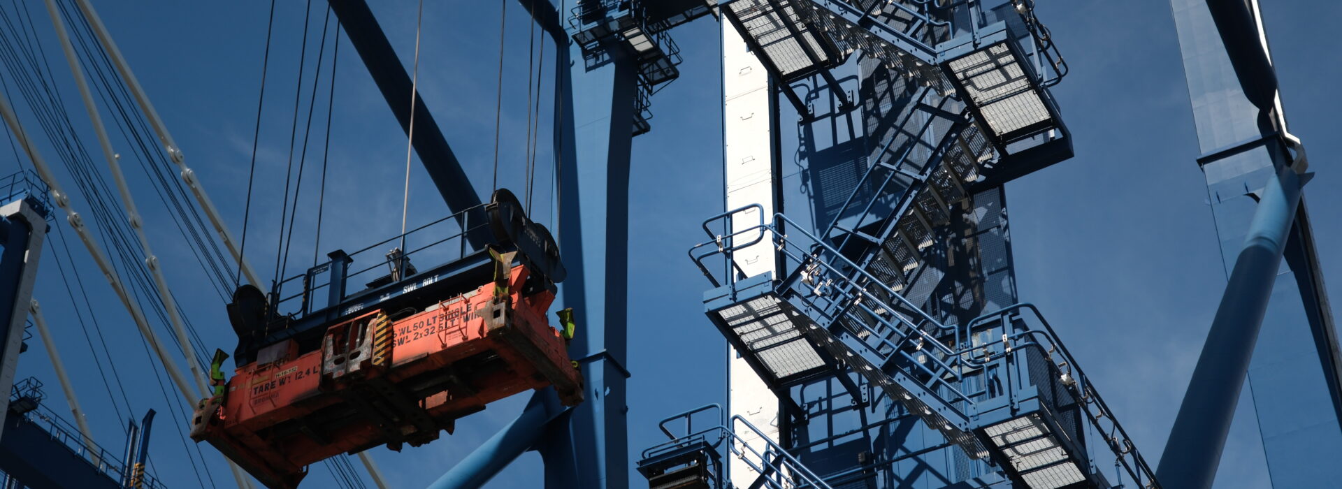 Detail of a port crane's lifting mechanism and steel structure against a blue sky.