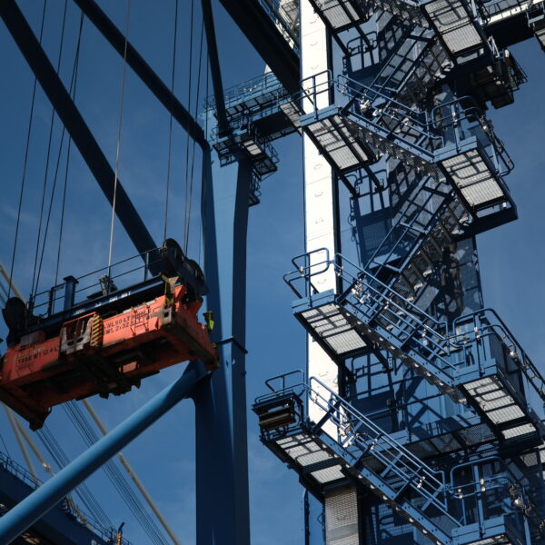 Detail of a port crane's lifting mechanism and steel structure against a blue sky.