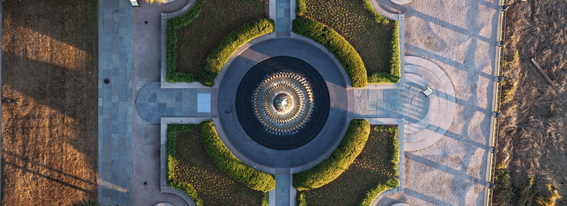 Top-down aerial view of a symmetrical formal garden with a circular fountain at its center.