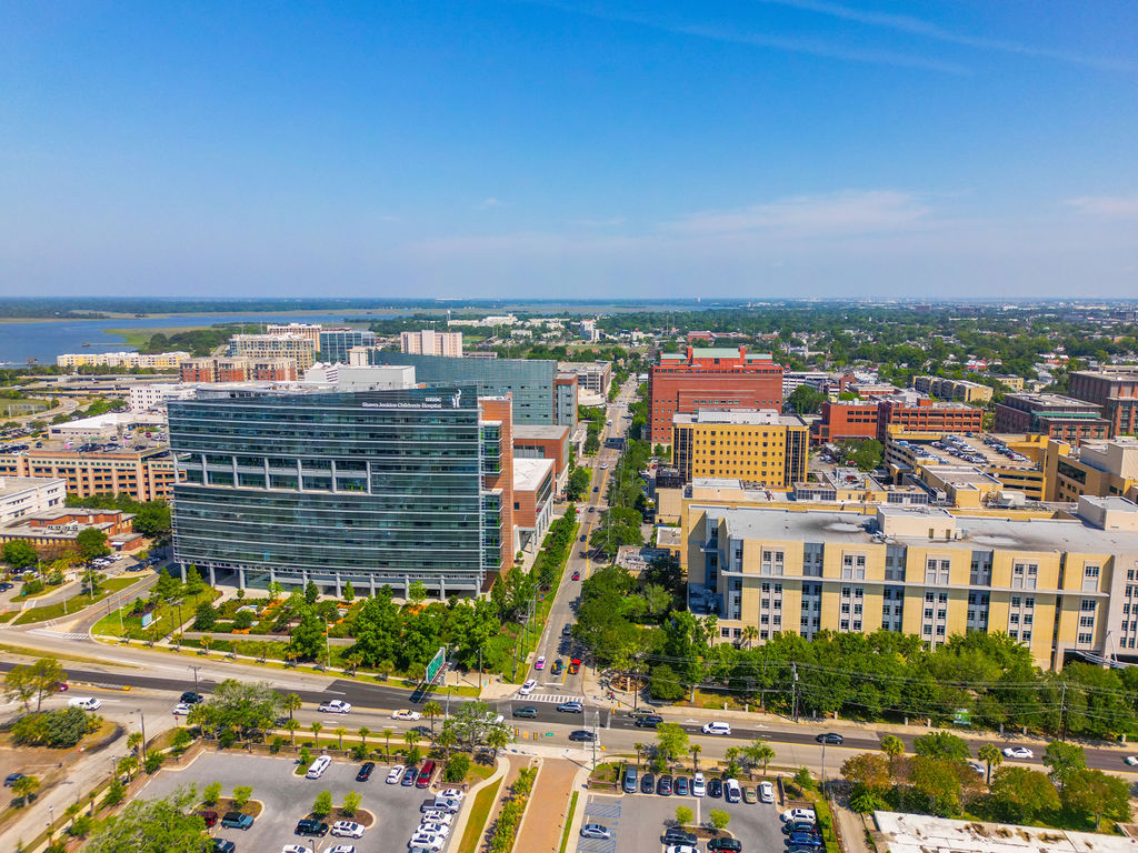Aerial view of a modern hospital complex and urban medical district with a waterfront in the background on a sunny day.