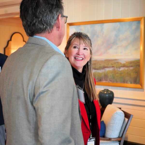 Woman in a red blazer smiling during a conversation with a man at an indoor event.