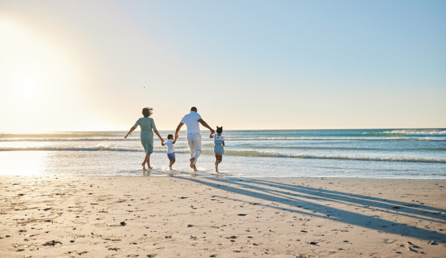Parents and two children walking toward the sea on a sandy beach at golden hour.