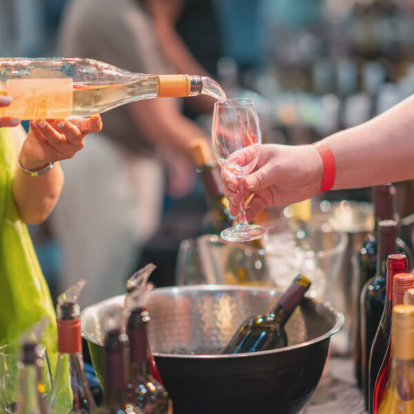 Wine pouring into glass at tasting counter with bartender serving wine to customer surrounded by multiple wine bottles in ice bucket. Wine tasting, hospitality business, alcohol service