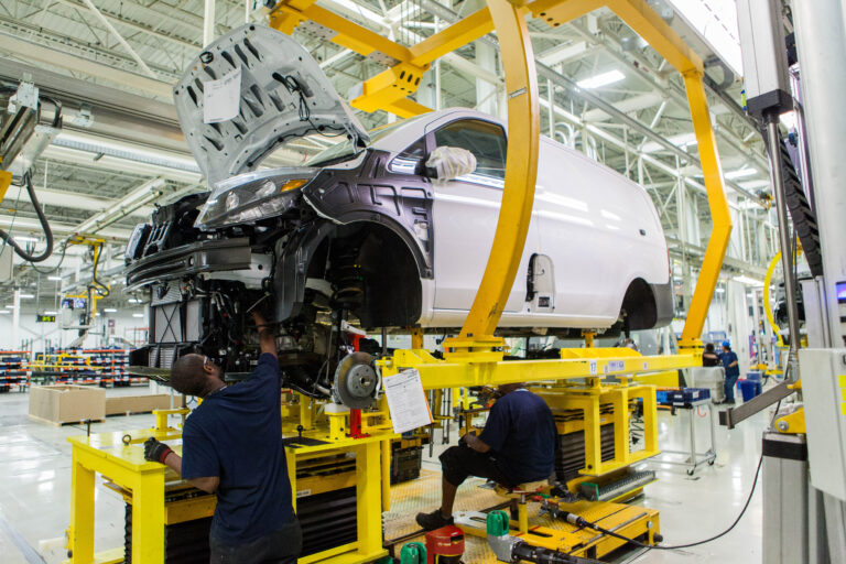A manufacturing employee works on the body of a car in a factory.