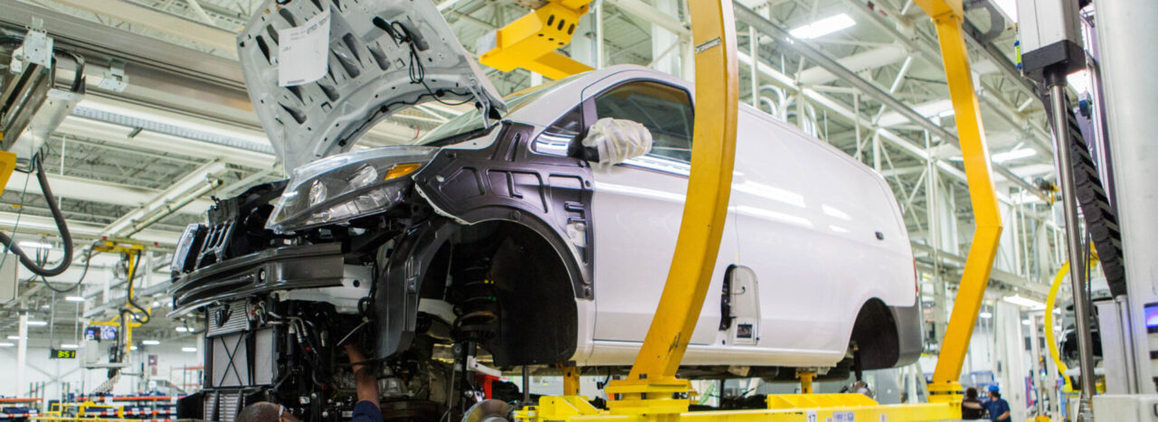 A manufacturing employee works on the body of a car in a factory.