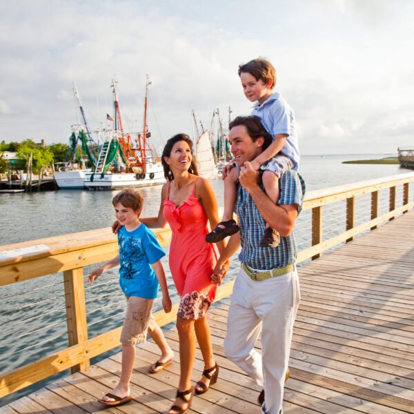 A family of four smiles as they walk down a boardwalk during the day.
