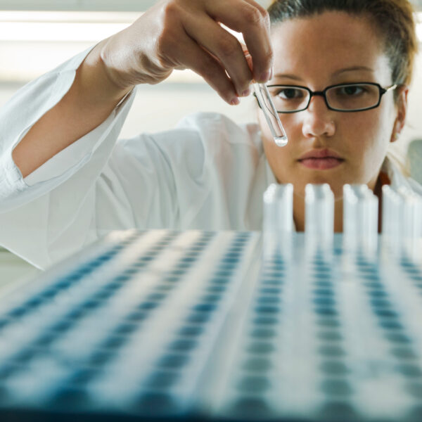 A scientist performs a quality assurance inspection on a series of test tubes.
