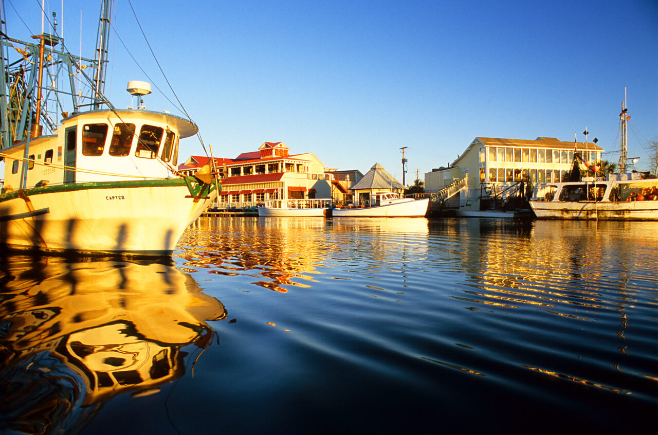 Boats at dock by a boardwalk at sunset.