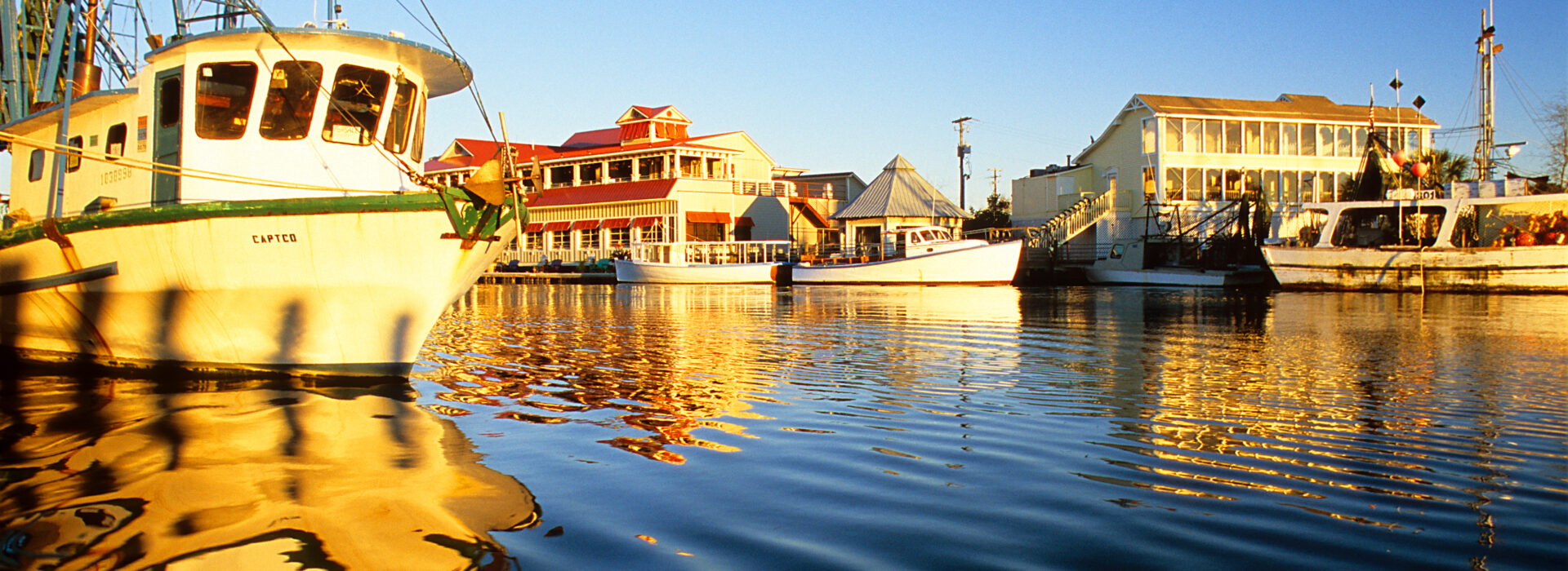 Boats at dock by a boardwalk at sunset.