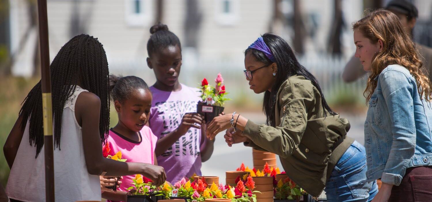 A group of women and children look at flowers at a farmer's market.