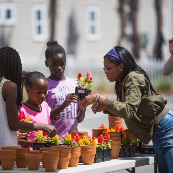 A group of women and children look at flowers at a farmer's market.