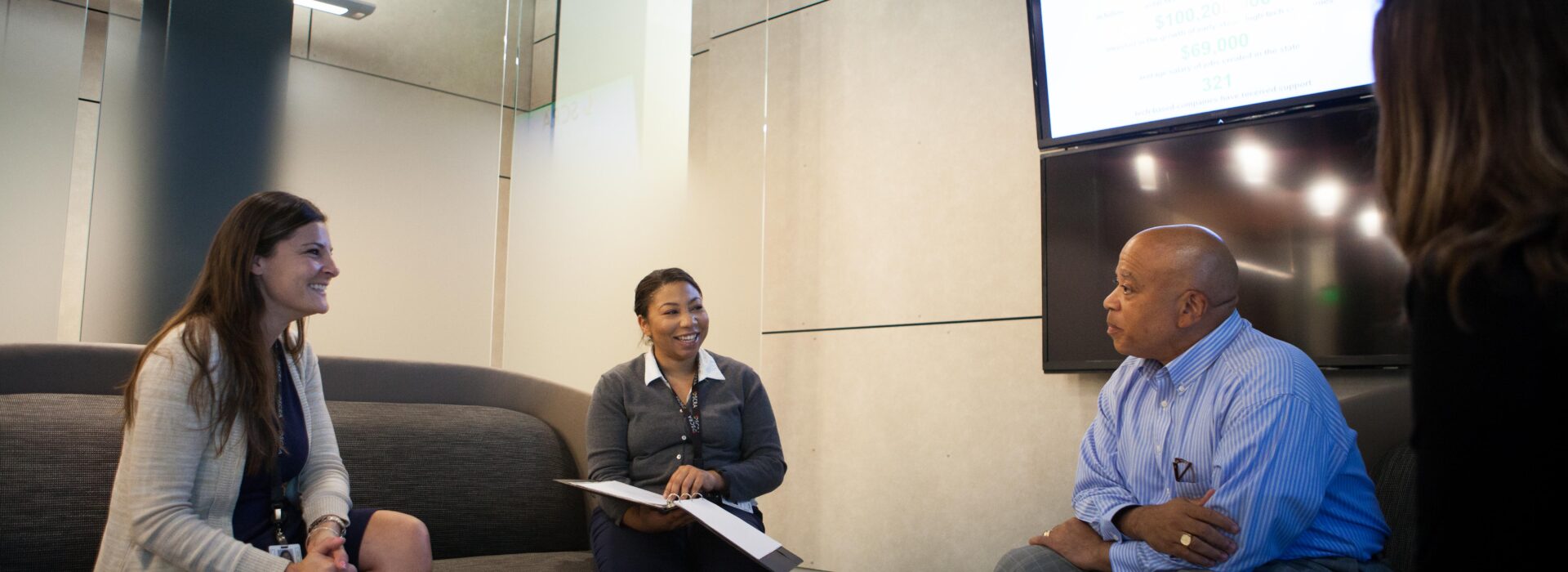 Three business people sit around a casual office table and talk together.