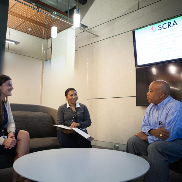 Three business people sit around a casual office table and talk together.